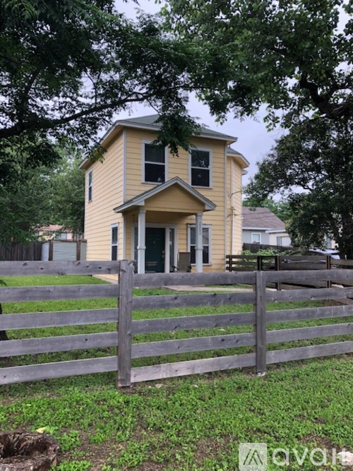 A yellow house with a grey fence in front of it.