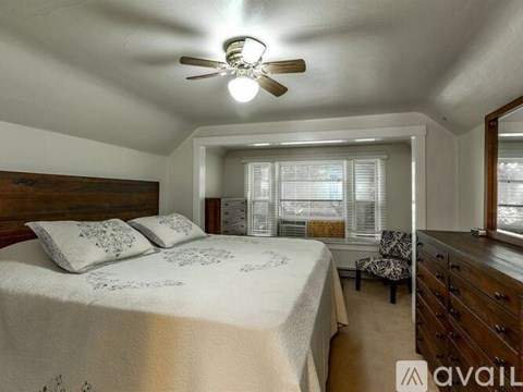 A bedroom with a bed, a chair, and a ceiling fan.