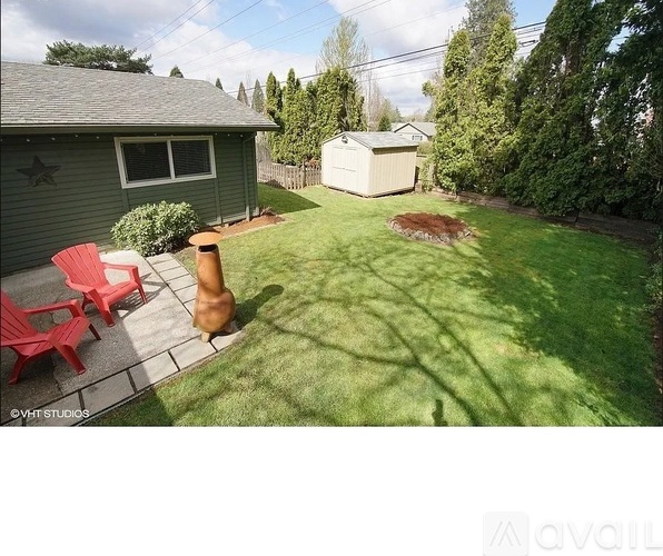 A backyard with a green lawn, a red chair, and a wooden post.