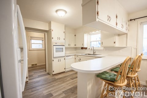 A kitchen with white cabinets and a white island with green cushions.