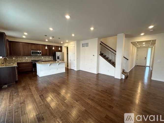 A spacious living room with hardwood floors and a staircase in the background.
