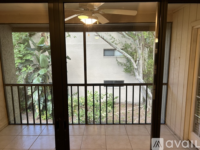 A balcony with a fan and a view of a building and trees.