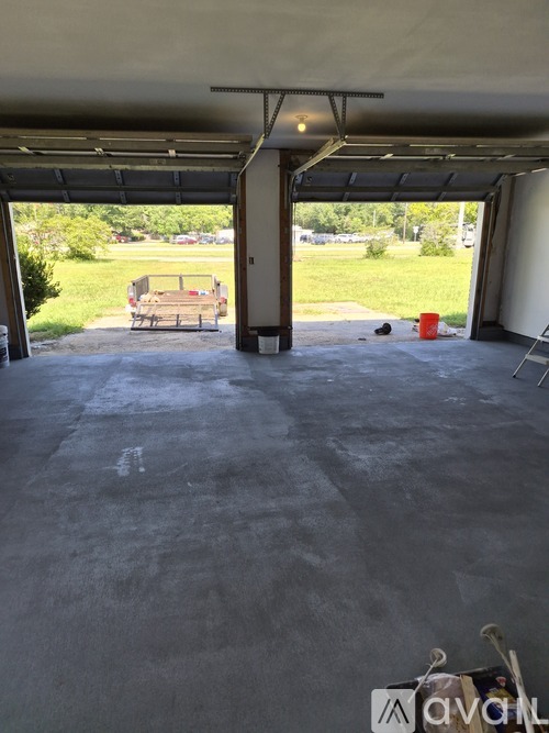 A large garage with a concrete floor and a doorway leading to a grassy area.
