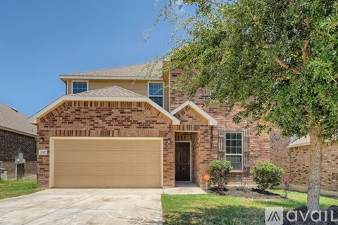 A brick house with a garage door and a tree in front.