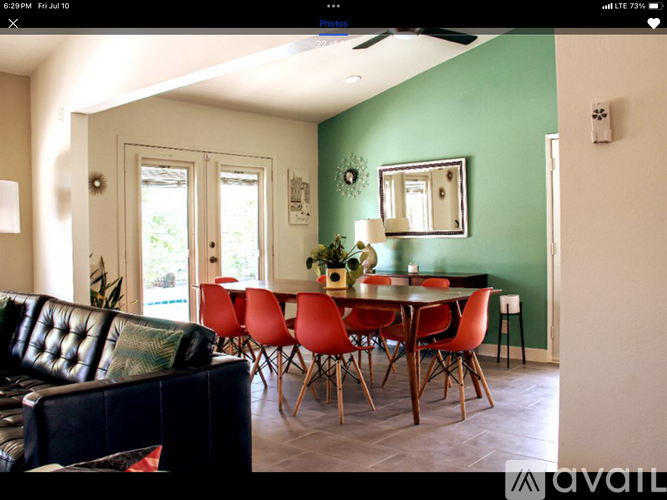 A living room with a black leather couch and a dining table with red chairs.