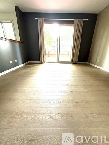 A spacious room with wooden flooring and a large doorway leading to a balcony.