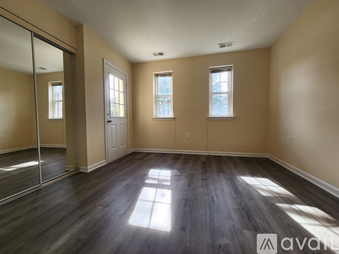 A spacious room with wooden floors and three windows allowing natural light to enter.