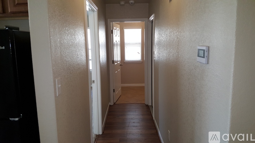 A hallway with a black refrigerator on the left and a door at the end.