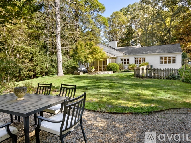 A white house with a black roof and a white picket fence is surrounded by trees.