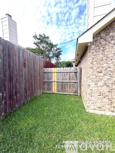 A wooden fence with a yellow stripe is in front of a brick building.