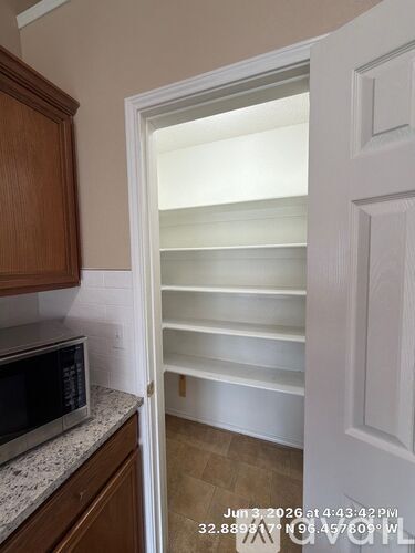 A kitchen with a microwave on the counter and an open door leading to a pantry.