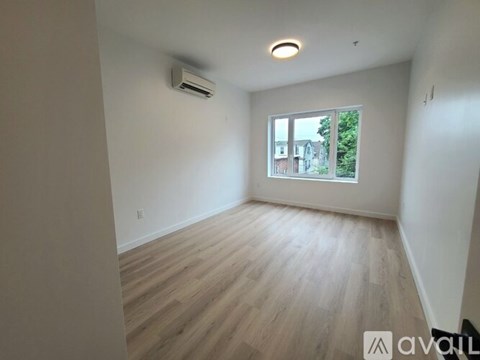 A room with wooden flooring and a window showing a view of buildings and trees outside.