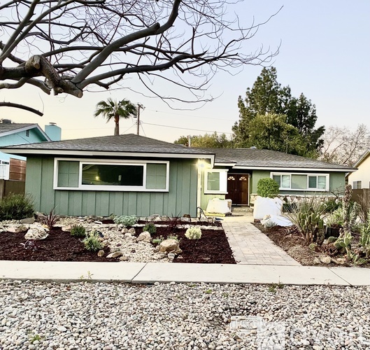 A house with a green exterior and a grey roof with a small front yard.