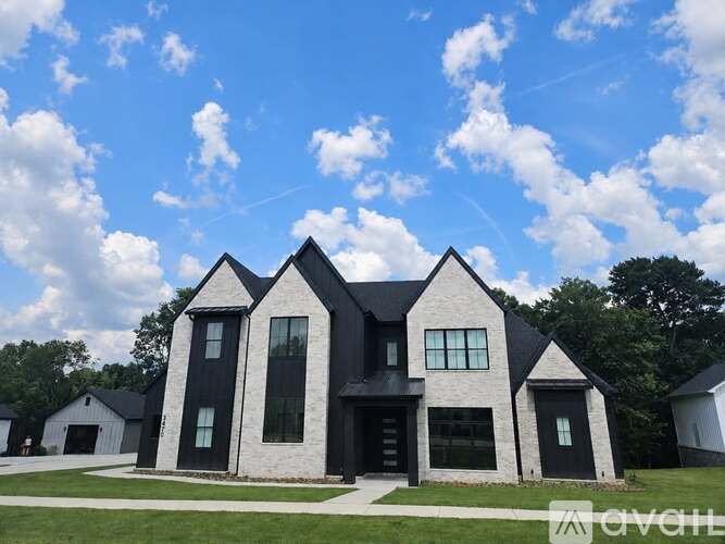 A modern house with black and white exterior is set against a blue sky with clouds.