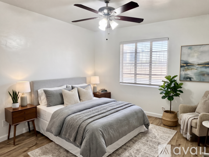 A bedroom with a large bed, a ceiling fan, and a window with blinds.