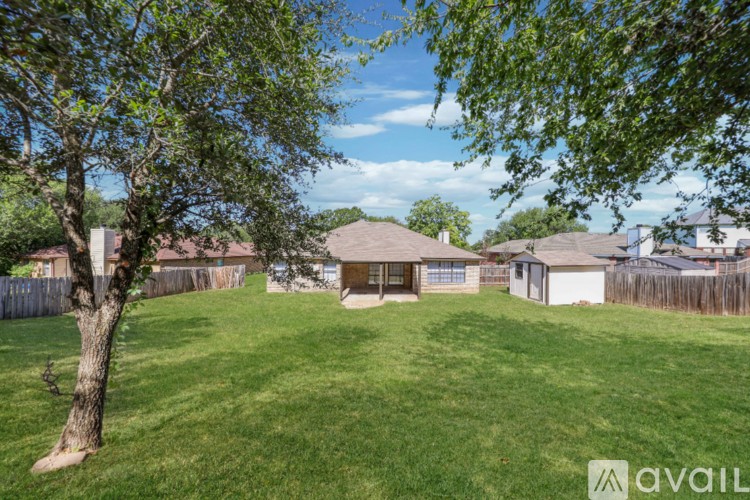 A tree is in the foreground of a grassy area with houses in the background.
