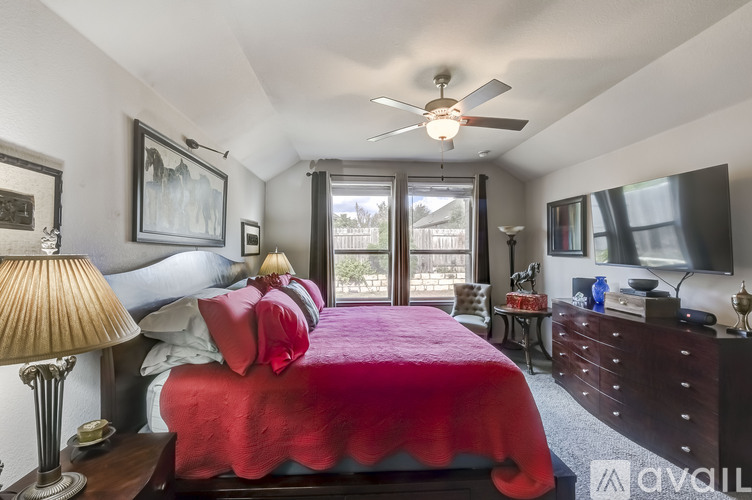 A bedroom with a red bedspread and a ceiling fan.