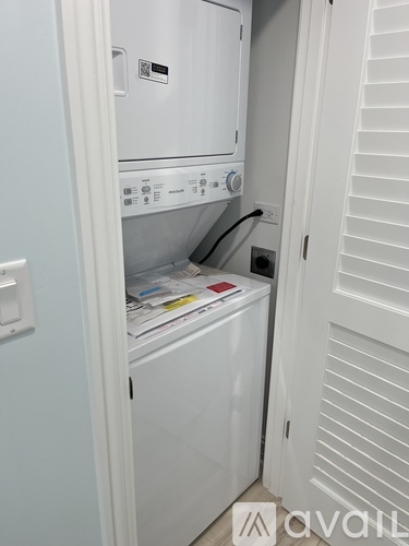 A white washing machine is in a small space between a wall and a door.