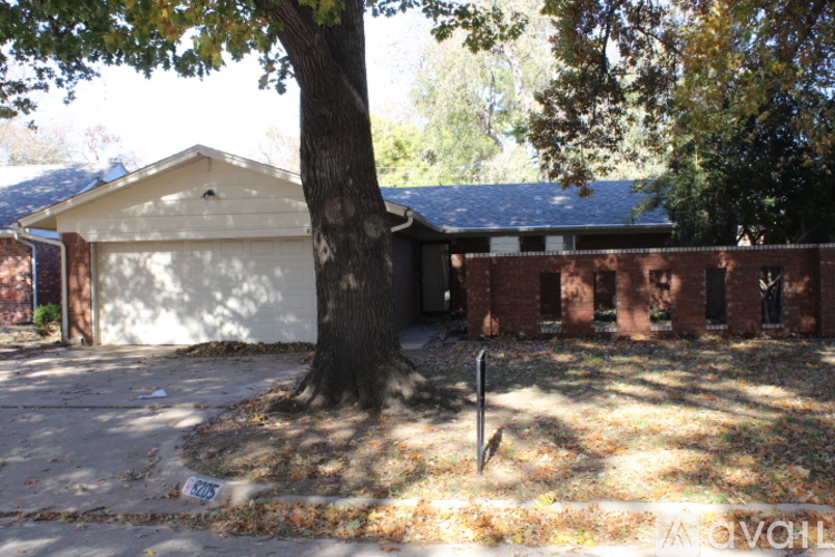 A tree in front of a house with a sign that says "For Sale".