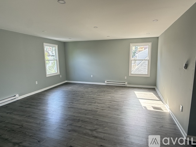 A spacious room with wooden flooring and two windows.
