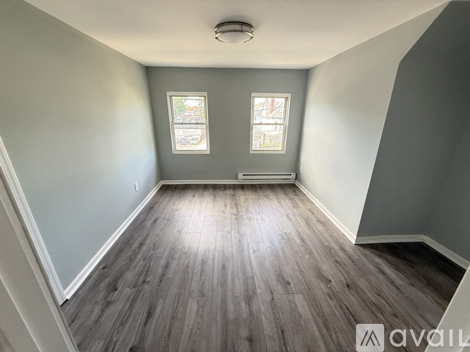 A room with wooden flooring and two windows.