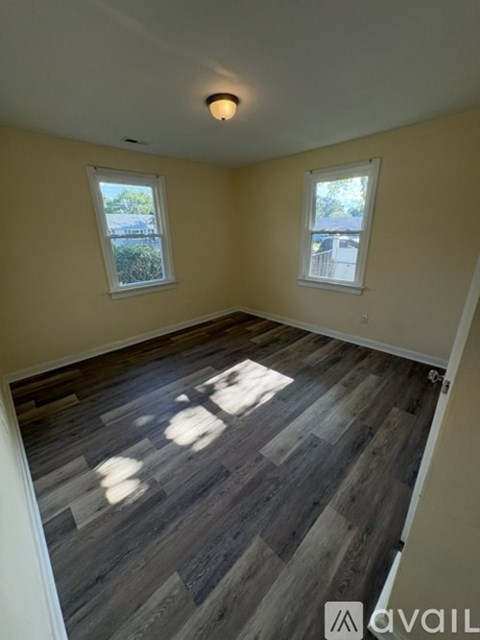 A room with wooden flooring and two windows.