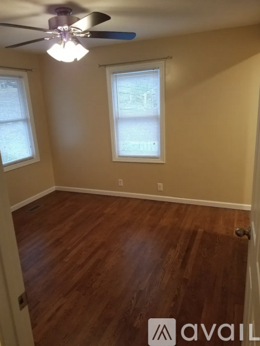 A room with a ceiling fan and two windows.