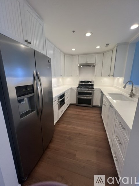 A modern kitchen with a stainless steel refrigerator and wooden flooring.
