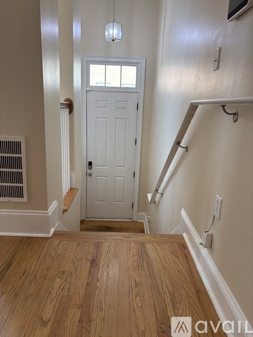 A white door is in a hallway with wood floors and a light hanging from the ceiling.