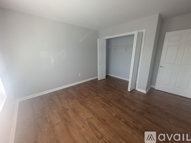 A room with wooden flooring and white walls, with a door and a window.
