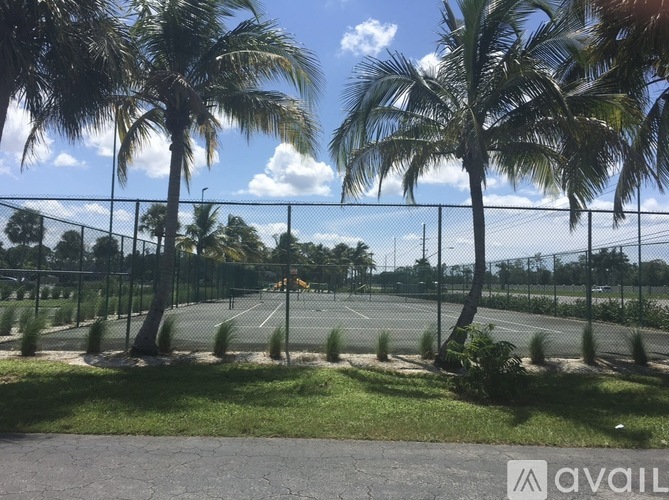 Tennis court surrounded by palm trees under a blue sky.