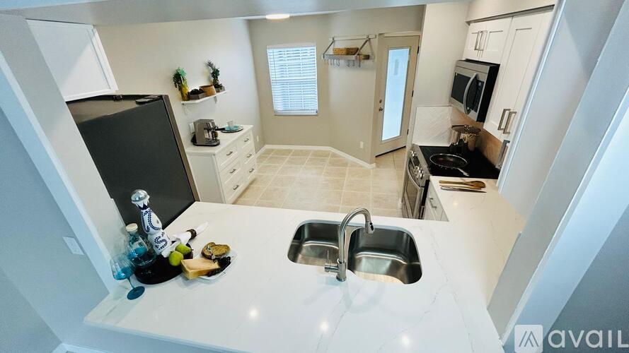 A kitchen with a black fridge, white countertops, and a white sink.