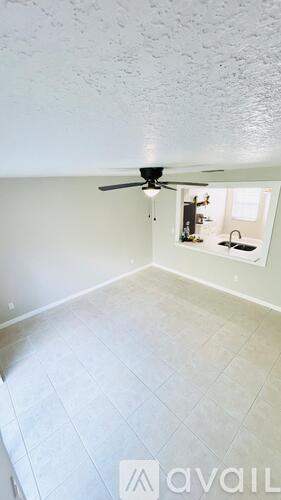A room with a ceiling fan and a kitchenette in the corner.
