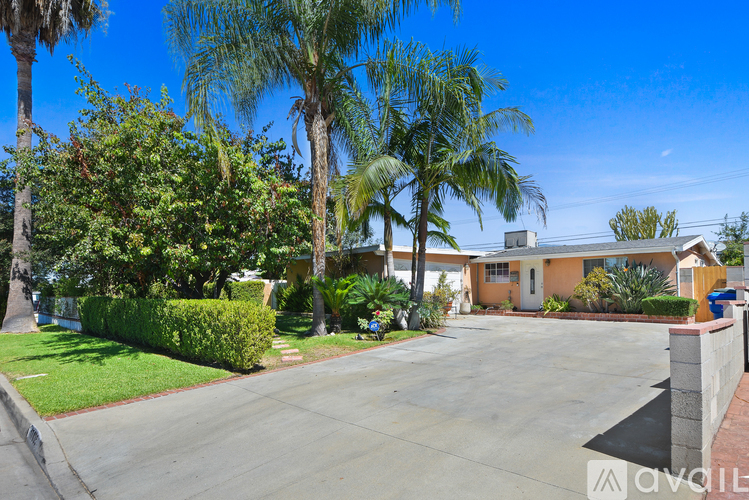 A house with a driveway surrounded by greenery and palm trees.