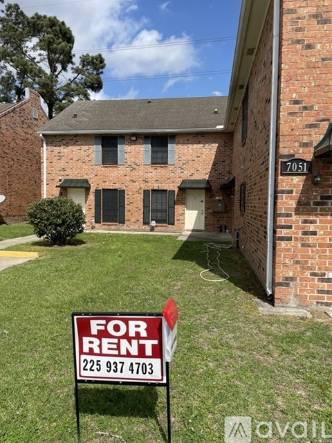 A red and white "For Rent" sign in front of a brick house.