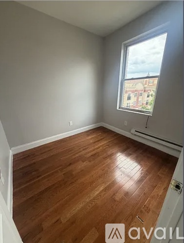 A room with wooden flooring and a window showing a view of a building outside.
