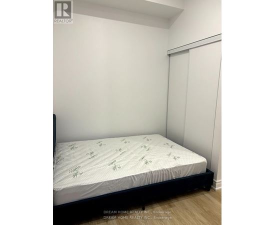 A bed with a white sheet and green palm tree pattern is in a room with a white wall and a door.