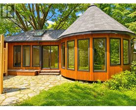A wooden gazebo with a black roof is surrounded by greenery.