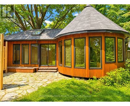 A wooden gazebo with a black roof is surrounded by greenery.