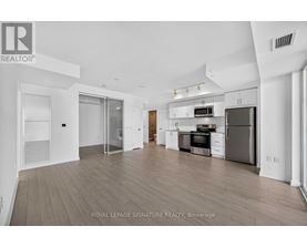 A spacious, well-lit kitchen and living room with wooden flooring and white walls.
