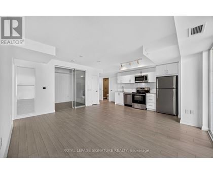 A spacious, well-lit kitchen and living room with wooden flooring and white walls.