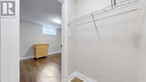 A room with a wooden floor and a white wall with a small window.