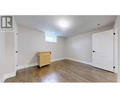 A room with a wooden floor and white walls, with a small window and a wooden cabinet.