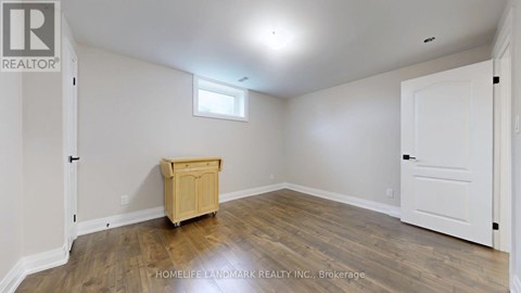 A room with a wooden floor and white walls, with a small window and a wooden cabinet.