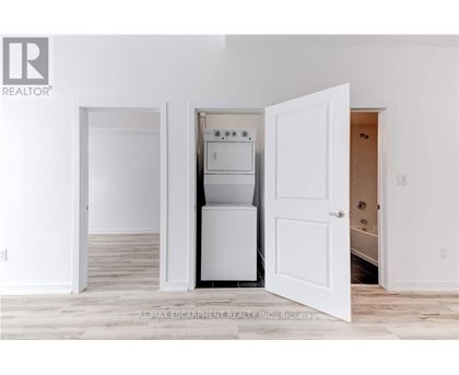 A white kitchen with a refrigerator, oven, and microwave in a room with white walls and wooden flooring.