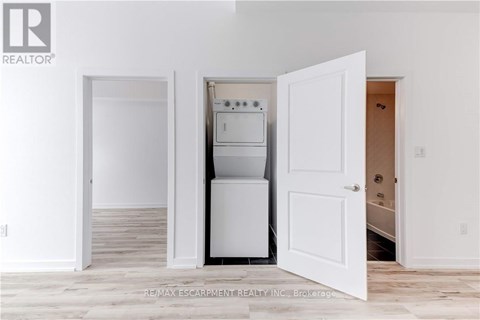 A white kitchen with a refrigerator, oven, and microwave in a room with white walls and wooden flooring.