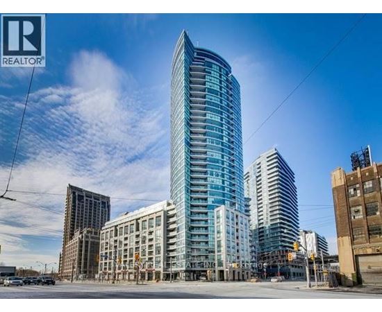 A tall, modern glass building stands in the foreground of a city street.