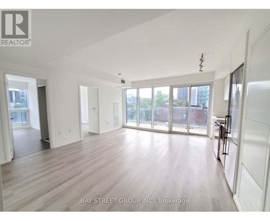 A spacious room with wooden flooring and large windows.