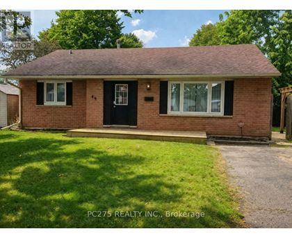 A house with a brown brick exterior and a black door is surrounded by greenery.
