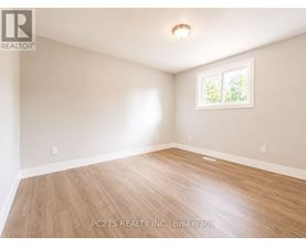 A room with wooden flooring and a window showing greenery outside.